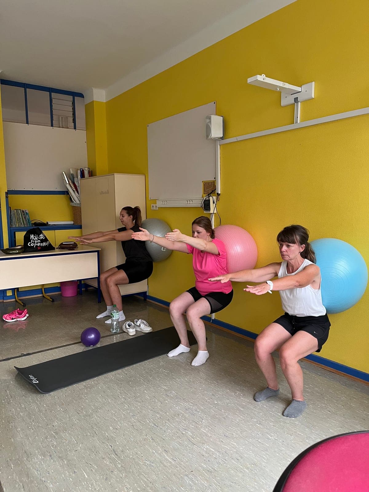 Cours collectif de Pilates : exercice debout avec swiss ball contre le mur